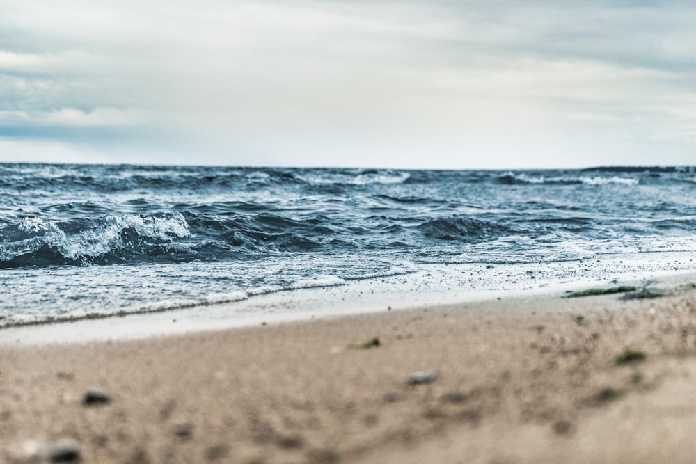 fotografia de baixo ângulo de areia marrom ao lado do corpo de água sob o céu branco e azul durante o dia