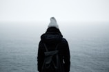 person wearing black jacket standing in front of the ocean