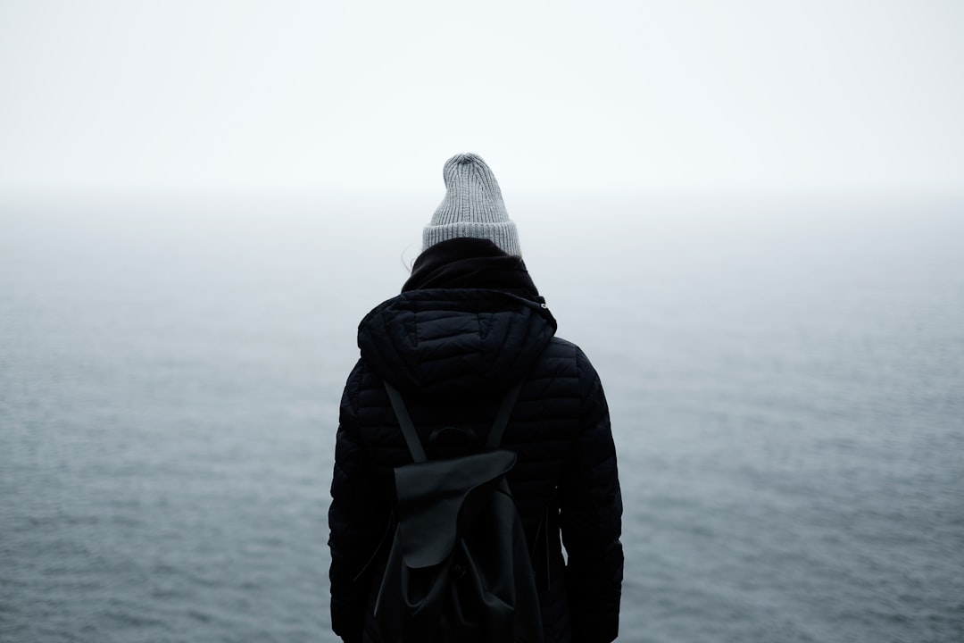 person wearing black jacket standing in front of the ocean