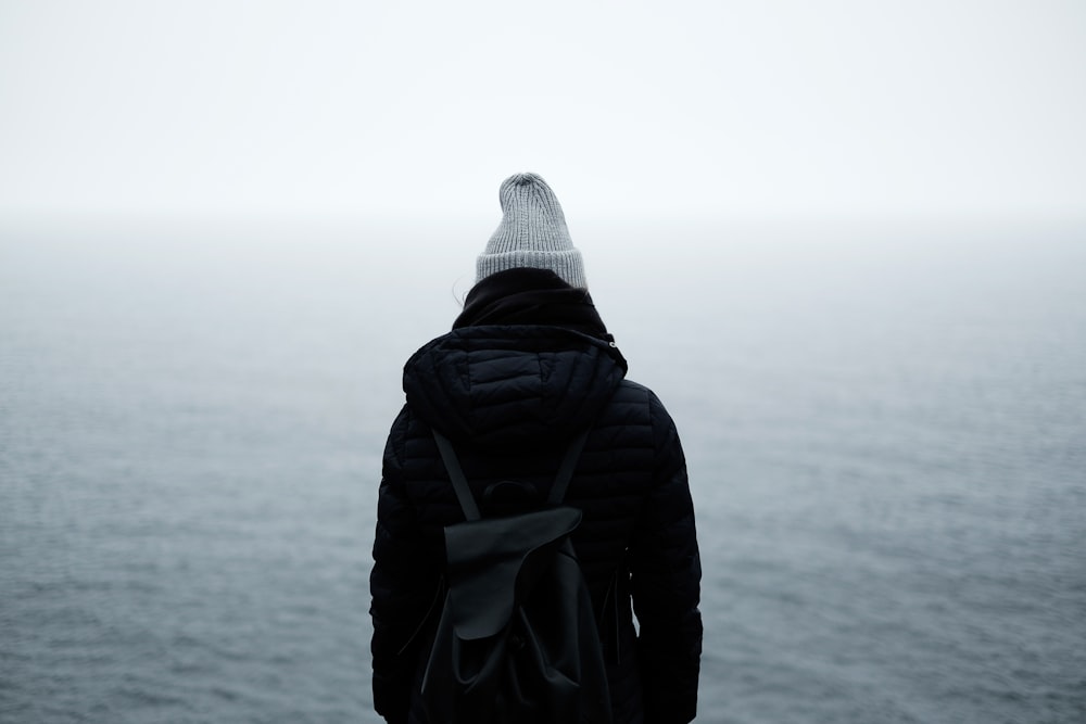 Person mit schwarzer Jacke, die vor dem Meer steht