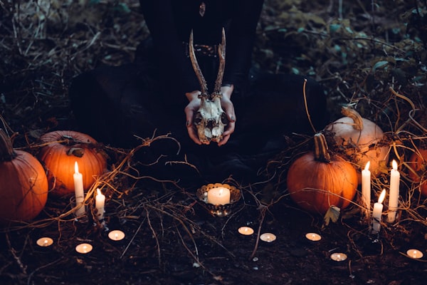 A person holding a skull around an outdoor altar, with pumpkins and candles all around.