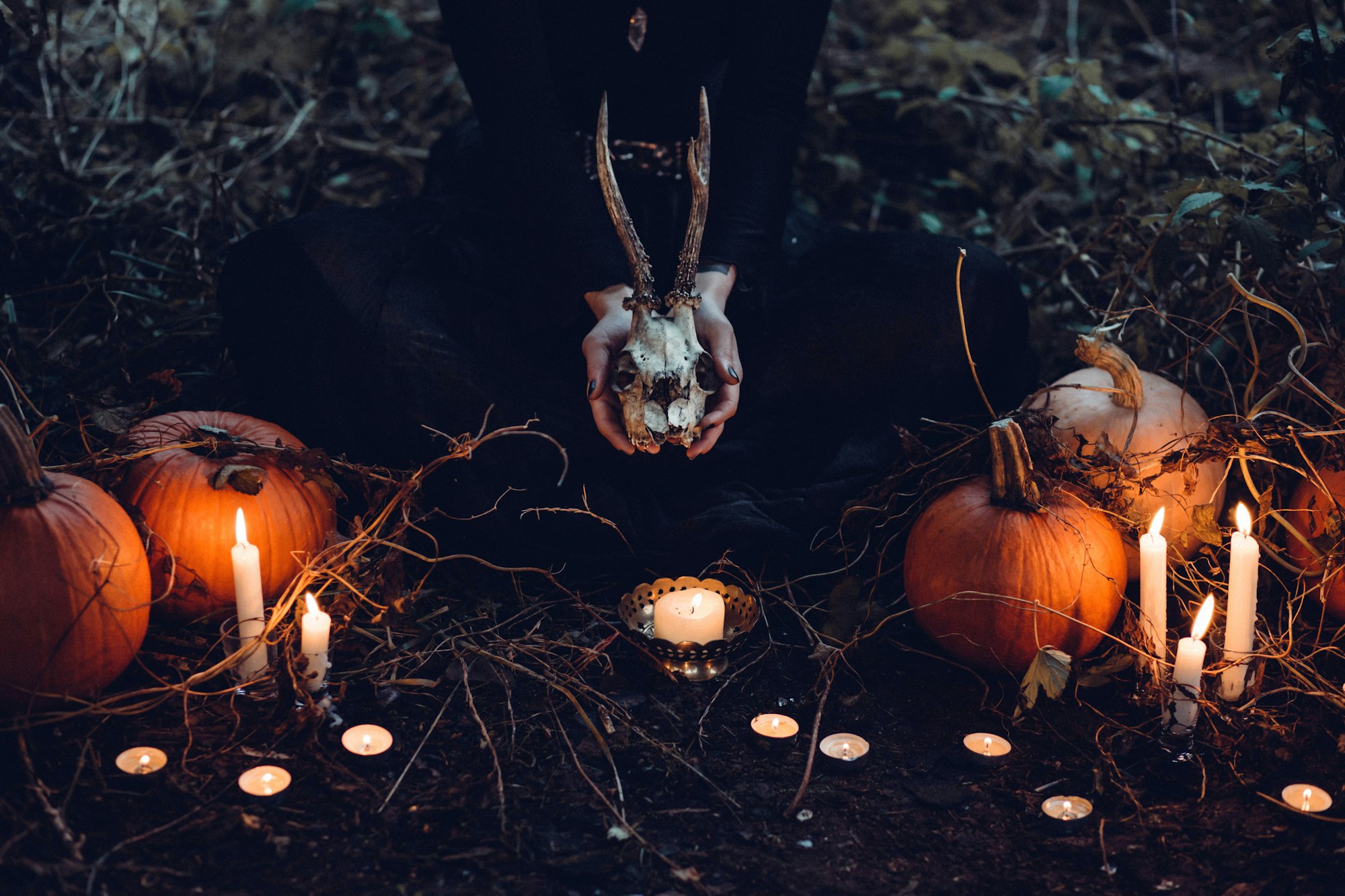 A person holding a skull around an outdoor altar, with pumpkins and candles all around.