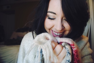 Woman holding a cozy knitted sweater, smiling while checking the fit in front of a mirror
