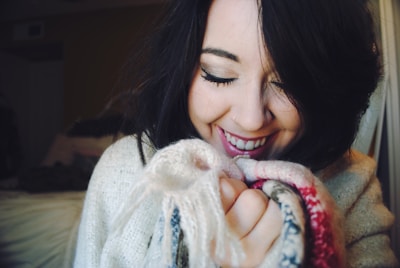 Woman holding a cozy knitted sweater, smiling while checking the fit in front of a mirror