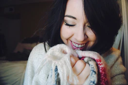 Smiling artisan gently holding a freshly made crochet sweater, bathed in natural light.