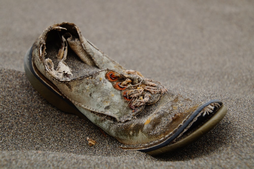 unpaariger brauner und schwarzer Schuh auf Sand