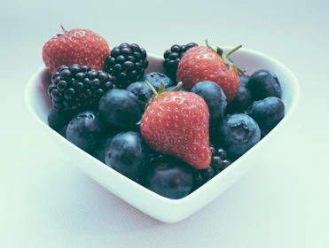 Close-up of a clay heart-shaped bowl with warm coral glaze, filled with fresh berries on a rustic linen cloth.