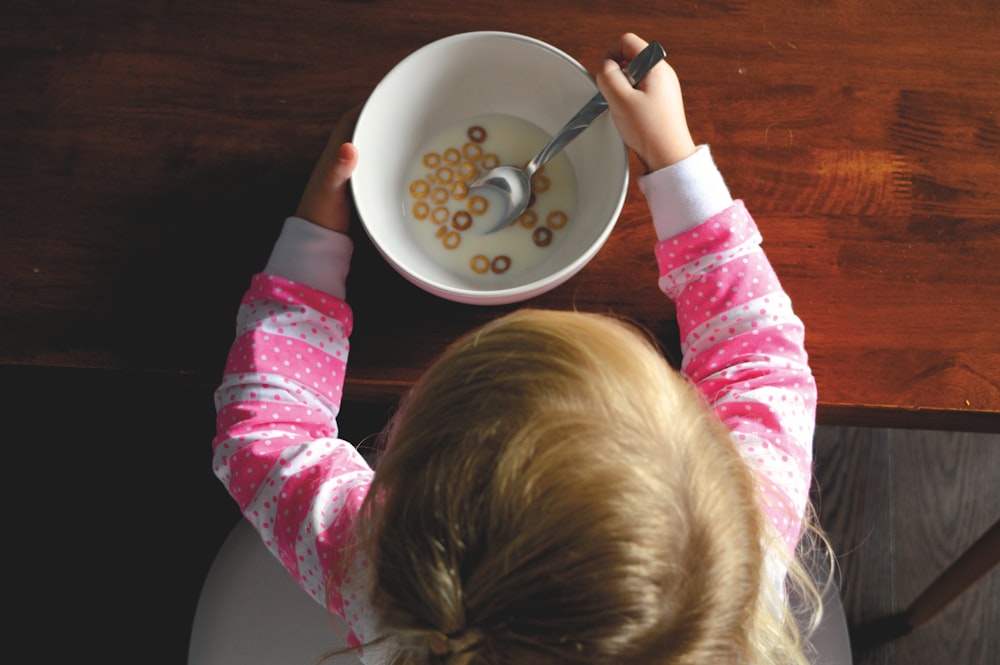 Mädchen, das Müsli in weißer Keramikschüssel auf dem Tisch isst