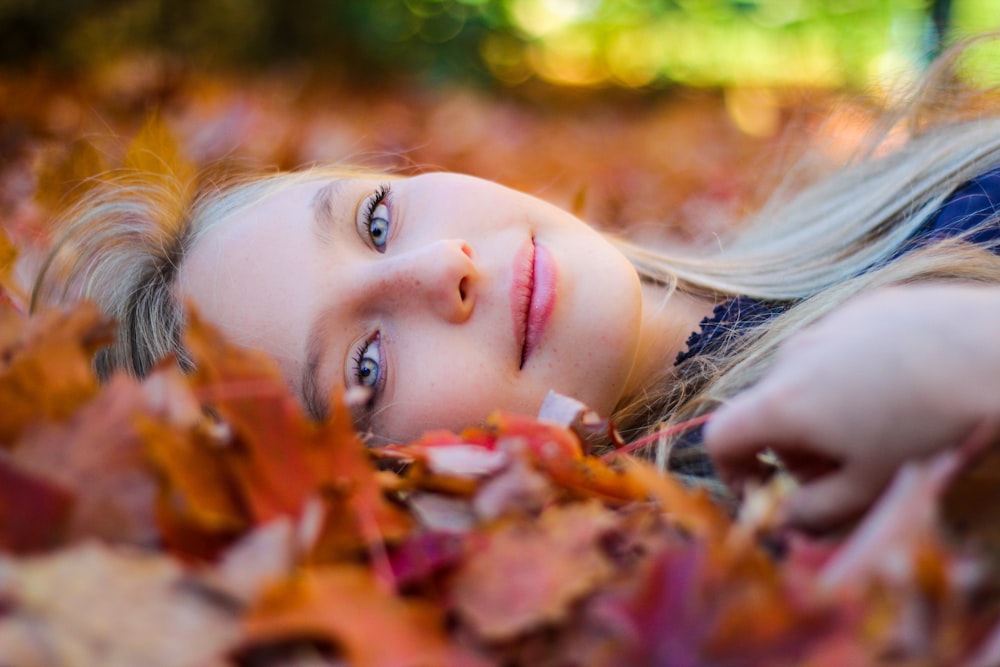 Femme portant un haut bleu allongée sur des feuilles d’érable séchées pendant la photographie de jour