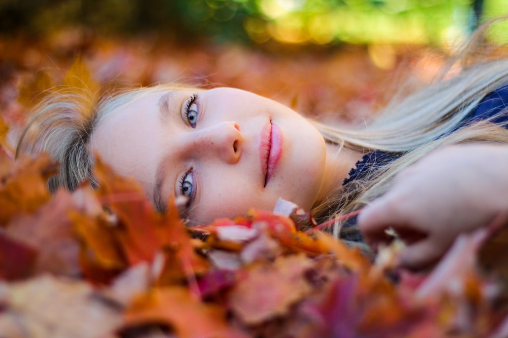 woman wearing blue top lying on dried maple leaves during daytime photography
