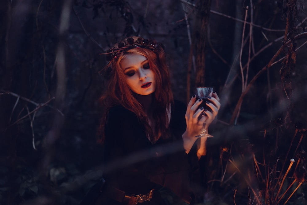 A girl in the woods holding a glass of wine on Halloween.