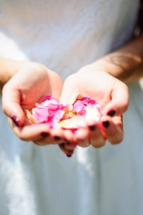 Hands resting peacefully on a soft white cloth with subtle pink petals nearby.