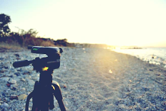 A sturdy tripod set up on a rocky surface overlooking a scenic sunset.
