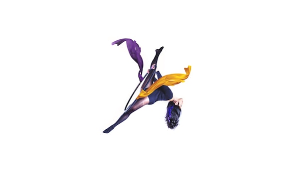 A person performs an acrobatic pose suspended in mid-air with a hoop. They are wearing a dark outfit with patterns or textures and have long dark hair. Flowing, colorful ribbons of purple and yellow accompany the motion of the pose, creating a dynamic and artistic effect.