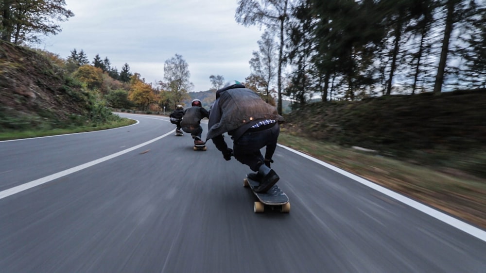 Tres personas montando patinetas cuesta abajo durante el día