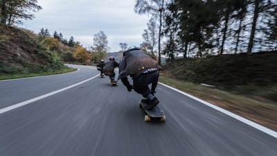 three person riding skateboards downhill during daytime extreme teams background