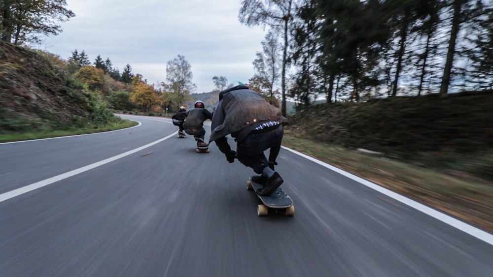 three person riding skateboards downhill during daytime