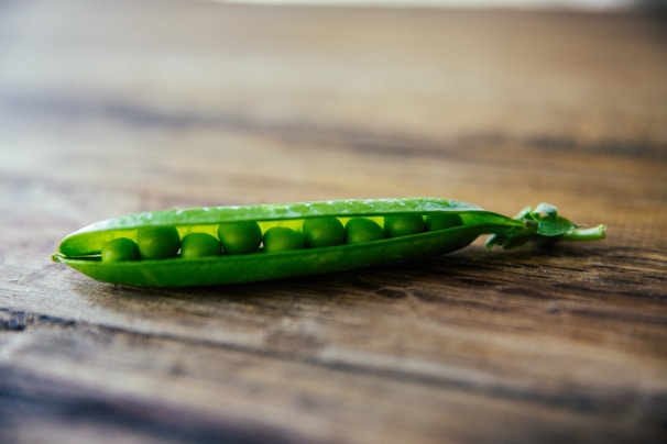 Bright green peas still in their pods on a rustic wooden surface