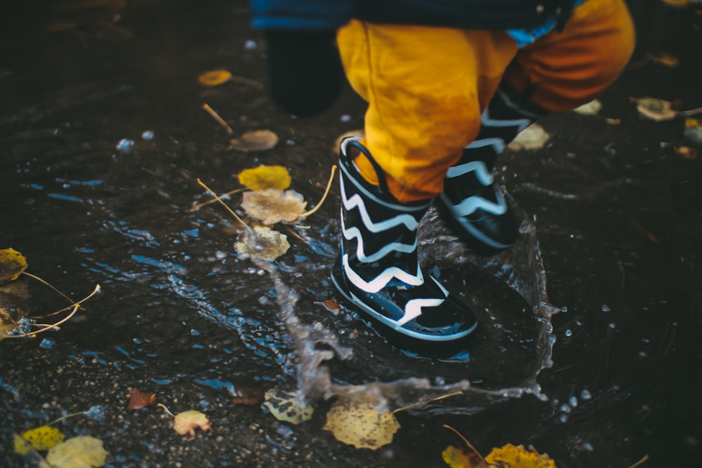 toddler wearing black and white rain boots standing on body of water