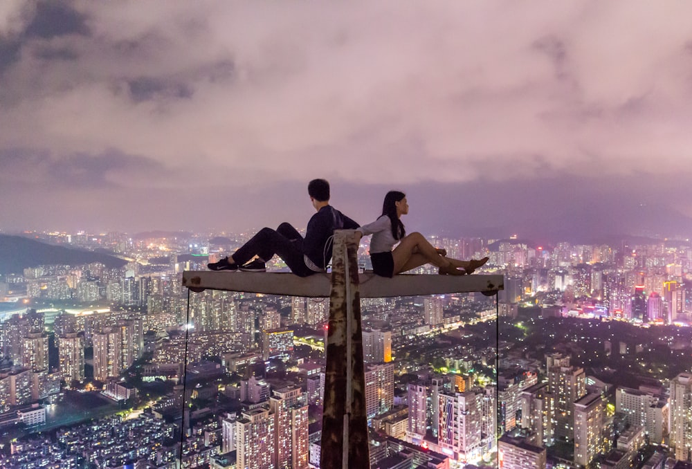 uomo e donna che si siedono sul metallo in cima al grattacielo