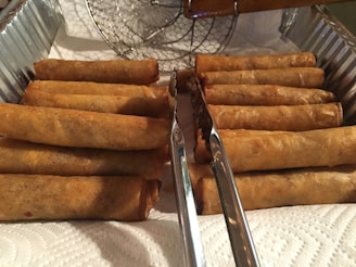 Rows of perfectly shaped vegetable and cheese spring rolls lined up on a stainless steel tray ready for packaging.