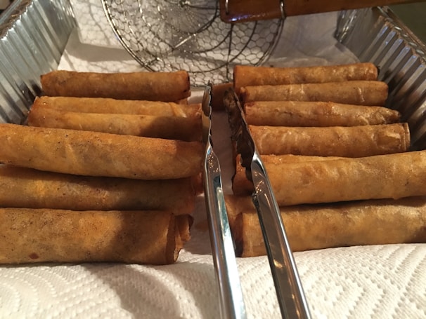 Rows of perfectly shaped vegetable and cheese spring rolls lined up on a stainless steel tray ready for packaging.