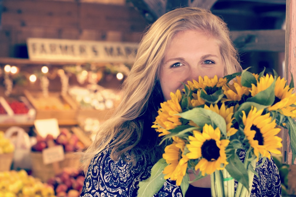 woman in blue and white floral top holding sunflower buoquet