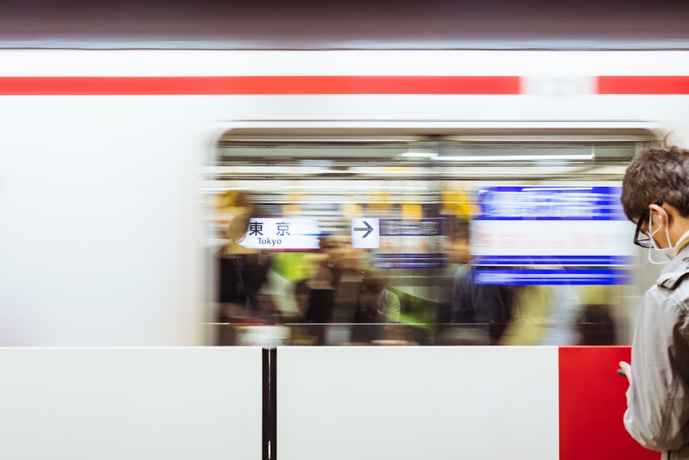 A blurry shot of a moving train in front of a man at the Tokyo Station.