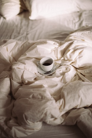 A sunlit morning outfit laid out on a cozy bed with soft linens and a cup of coffee nearby.