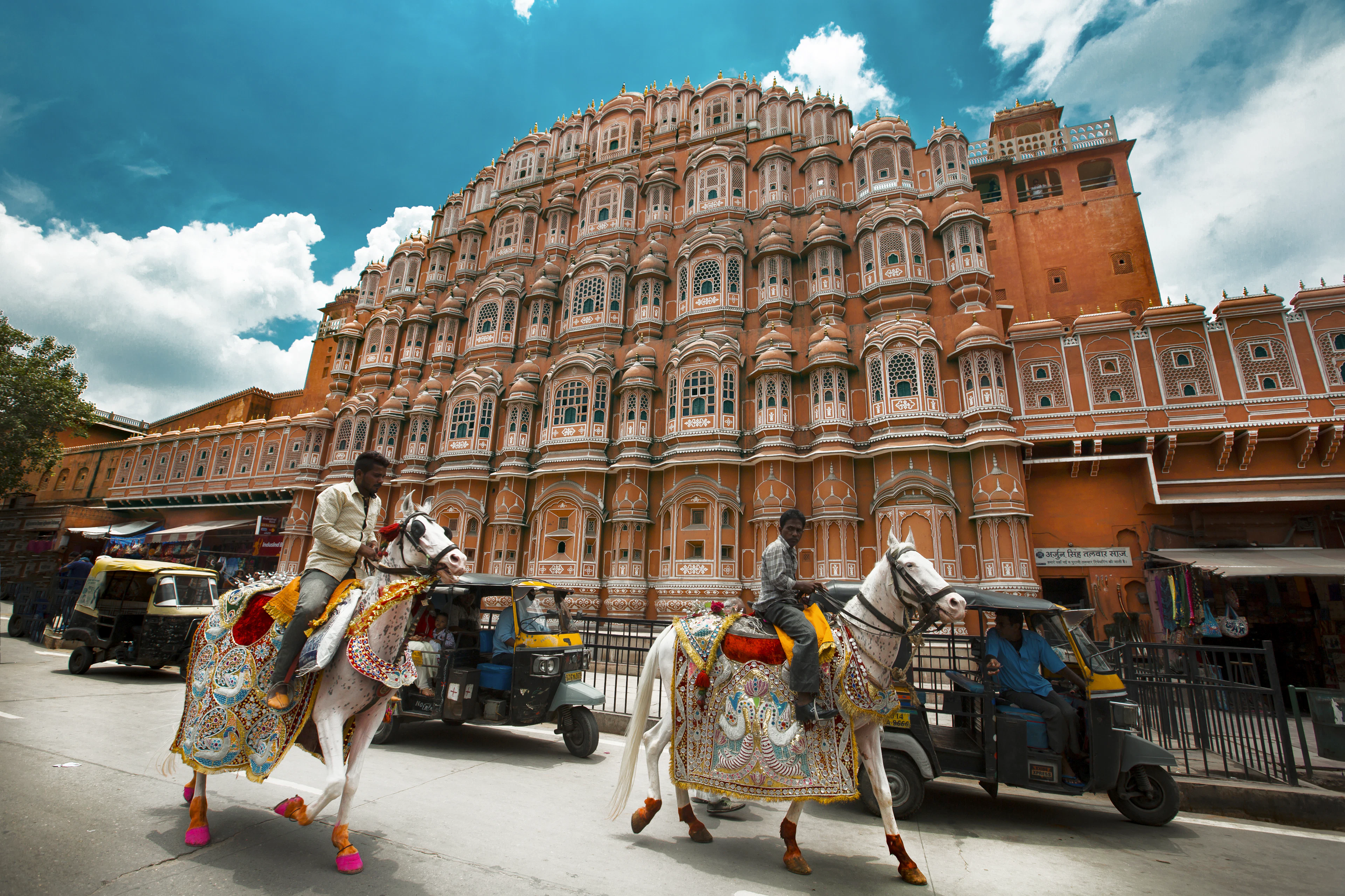 Riders on decorated white horses passing Hawa Mahal in Jaipur