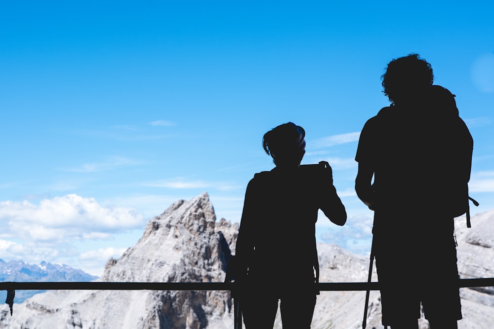 Fotografia da silhueta de duas pessoas em pé no topo sob o céu azul claro