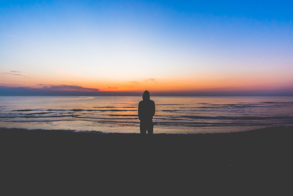 silhouette di persona in piedi vicino al mare durante l'ora d'oro