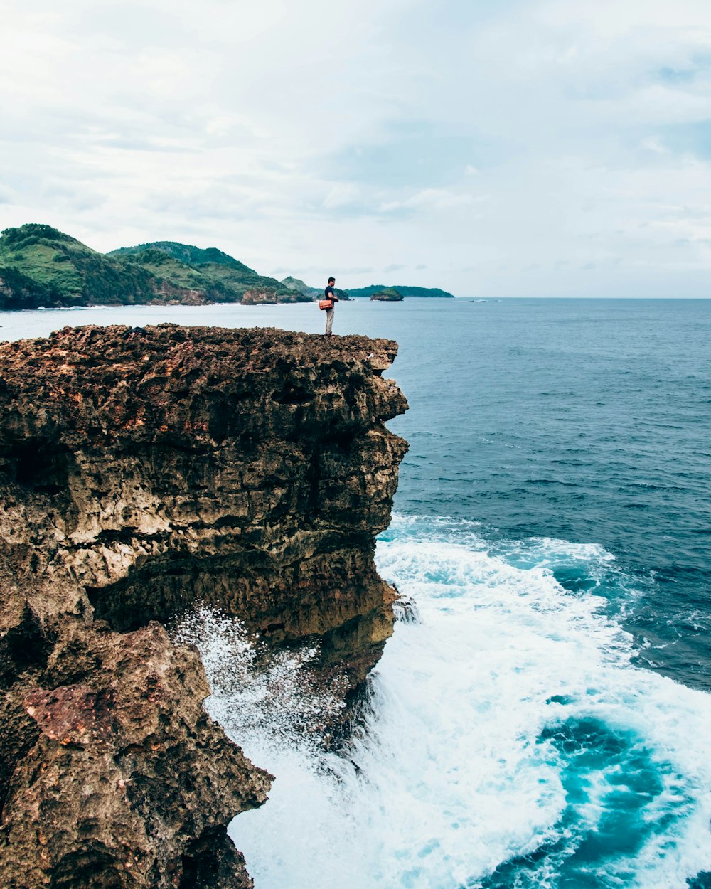 Person, die tagsüber auf einer grauen Felsformation neben einem Gewässer steht