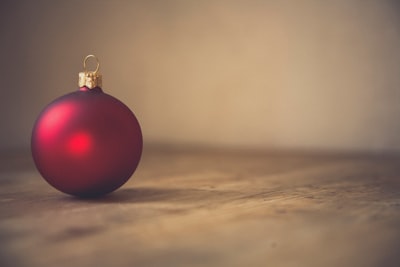 closeup photo of red ball ornament on surface holly teams background