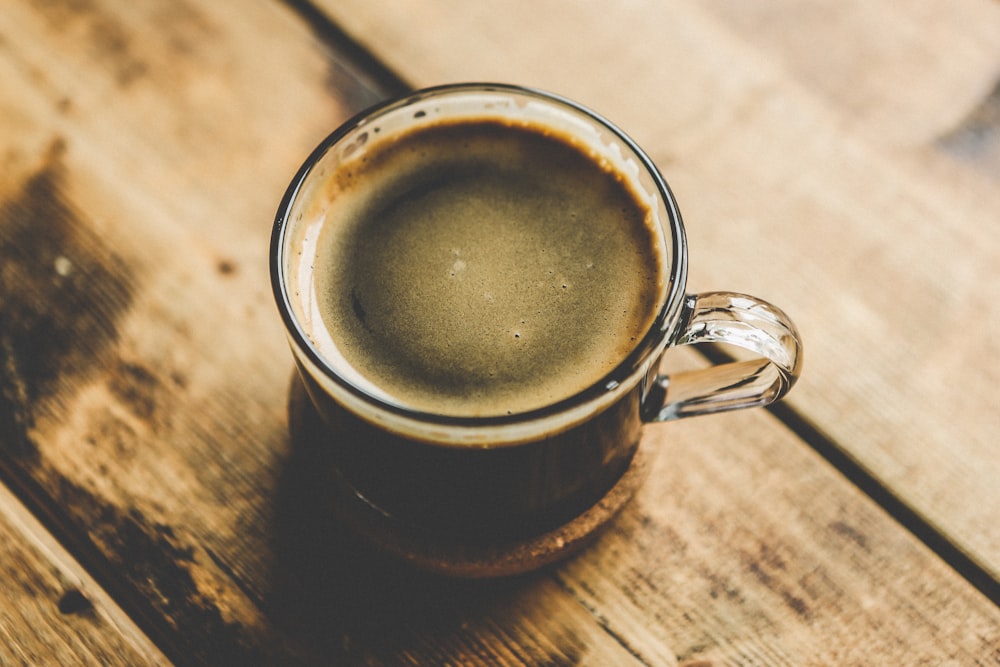 café noir dans une tasse à thé en verre sur une surface en bois brun