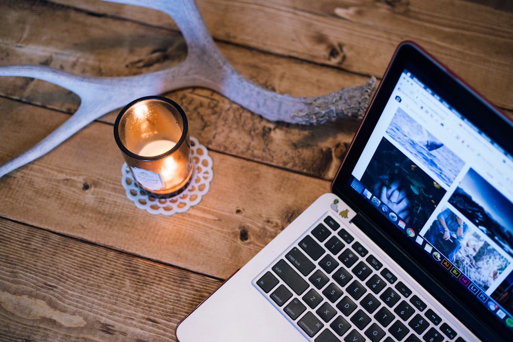 A lit candle and an antler on a table next to a laptop