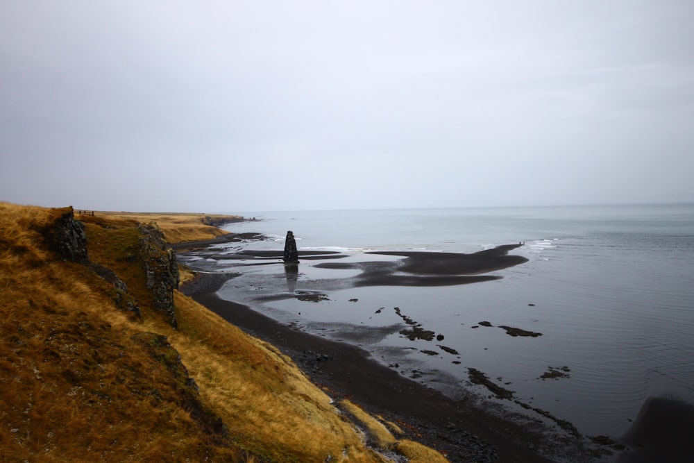 brown mountain near seashore under cloudy sky