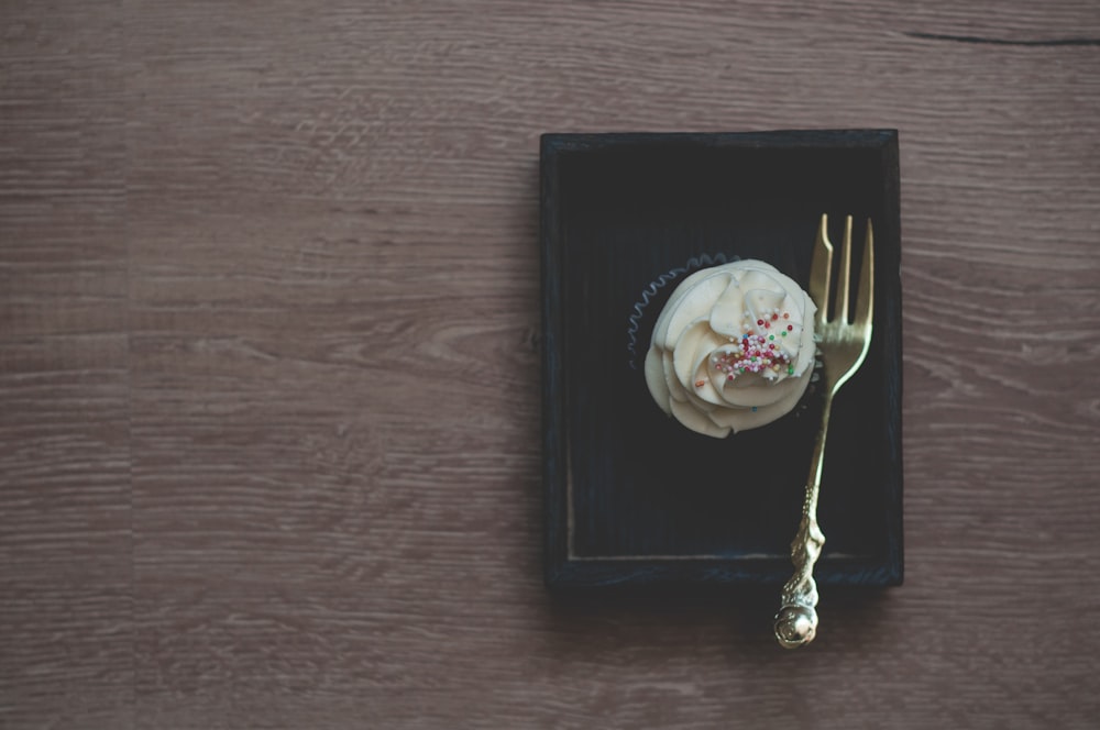 brass-colored pastry fork on black box beside cupcake with white frosting