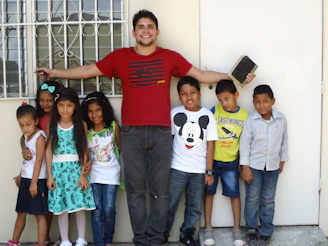 A group of smiling children gathered around a mentor reading books outdoors.