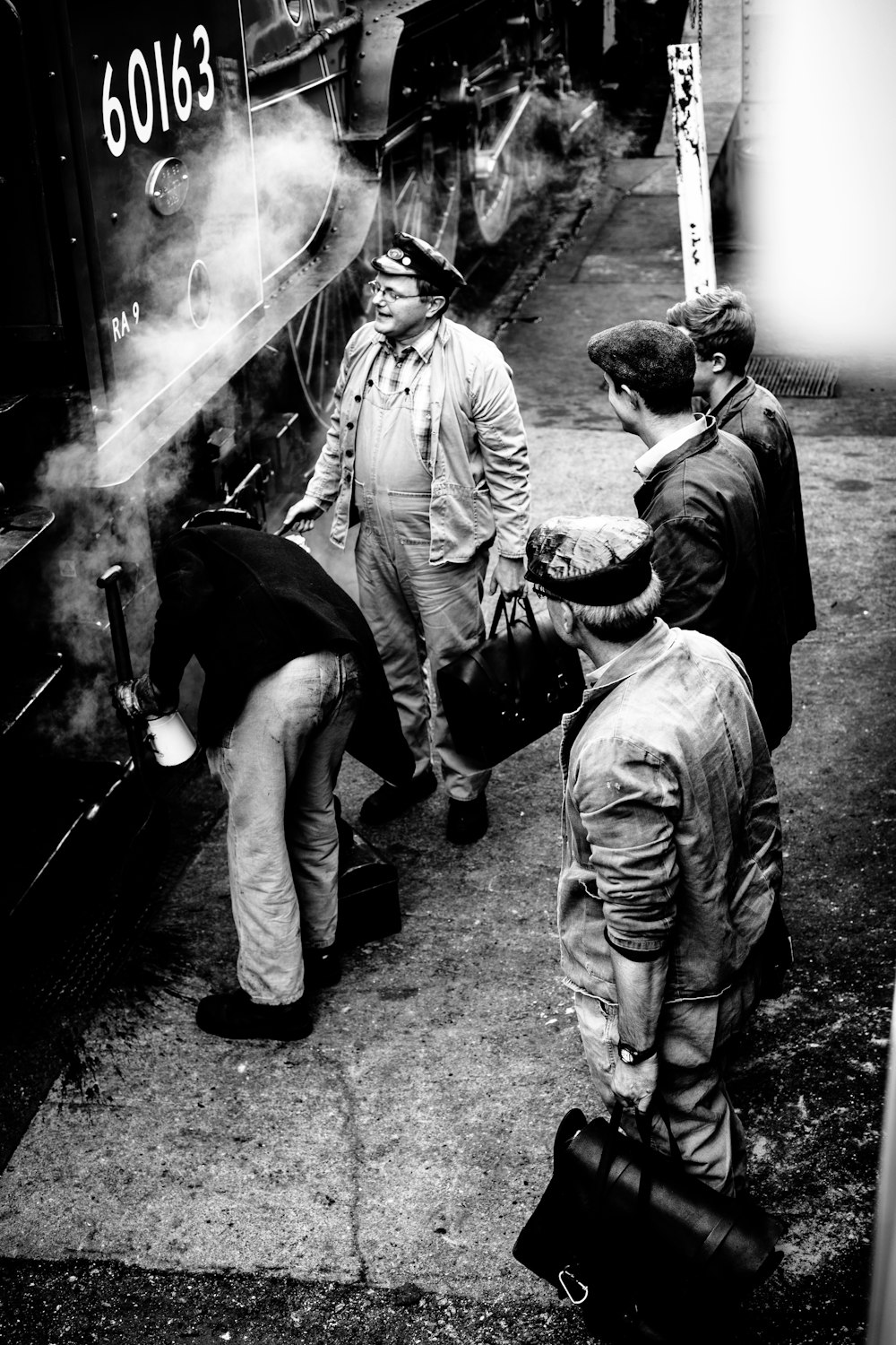 grayscale photo of men standing beside 60163 train
