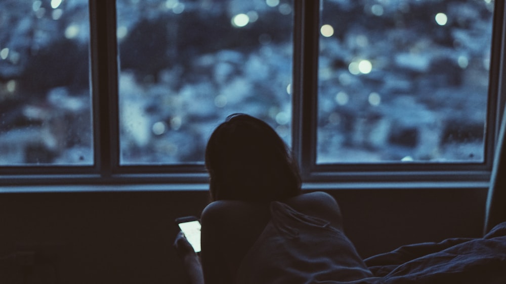 woman holding phone near window during daytime