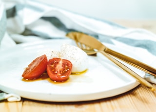 sliced tomato and mozzarella cheese on white plate beside brass-colored knife and fork