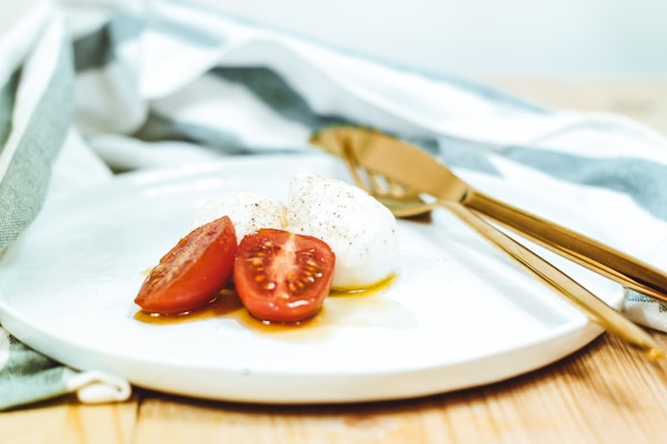 Sliced tomato and mozzarella cheese on white plate beside brass-colored knife and fork