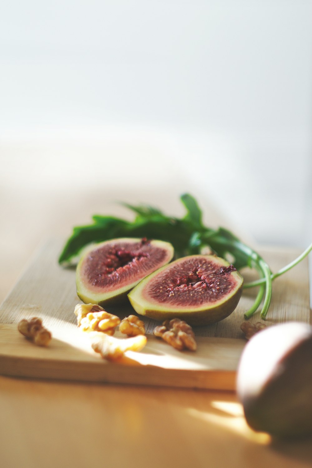 Cutting board with a fig fruit cut in half, a sprig of arugula, and walnuts