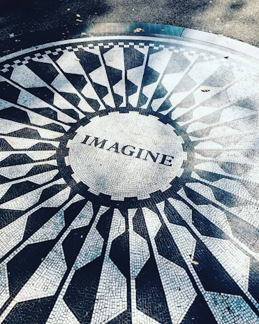 Mosaic pavement featuring the word 'IMAGINE' at its center, surrounded by a circular pattern of geometric shapes in black and white.