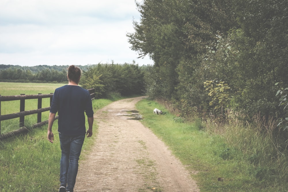 a man walking down a dirt road next to a lush green field