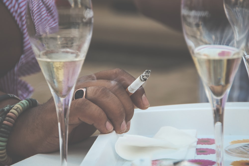 una persona sentada en una mesa con copas de vino y un cigarrillo