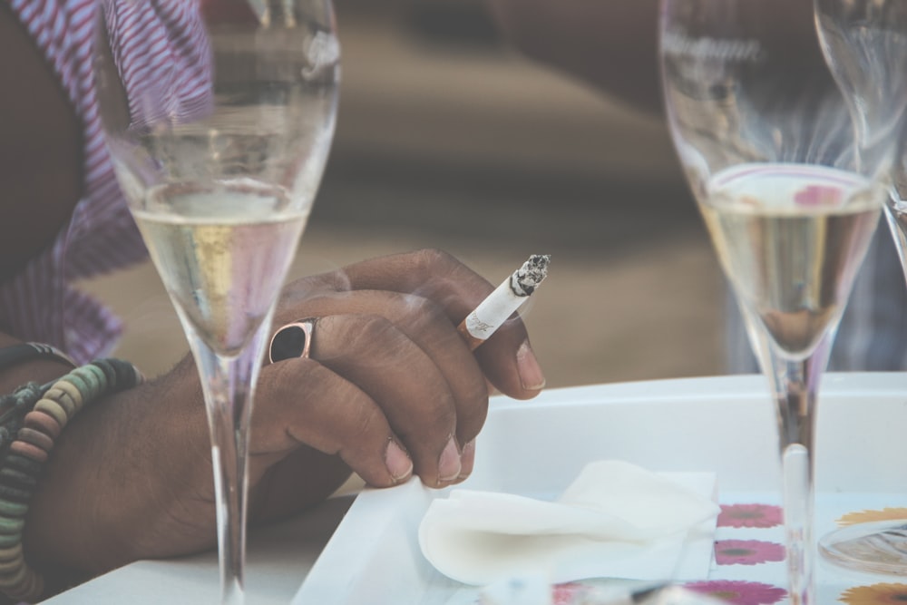 a person sitting at a table with wine glasses and a cigarette