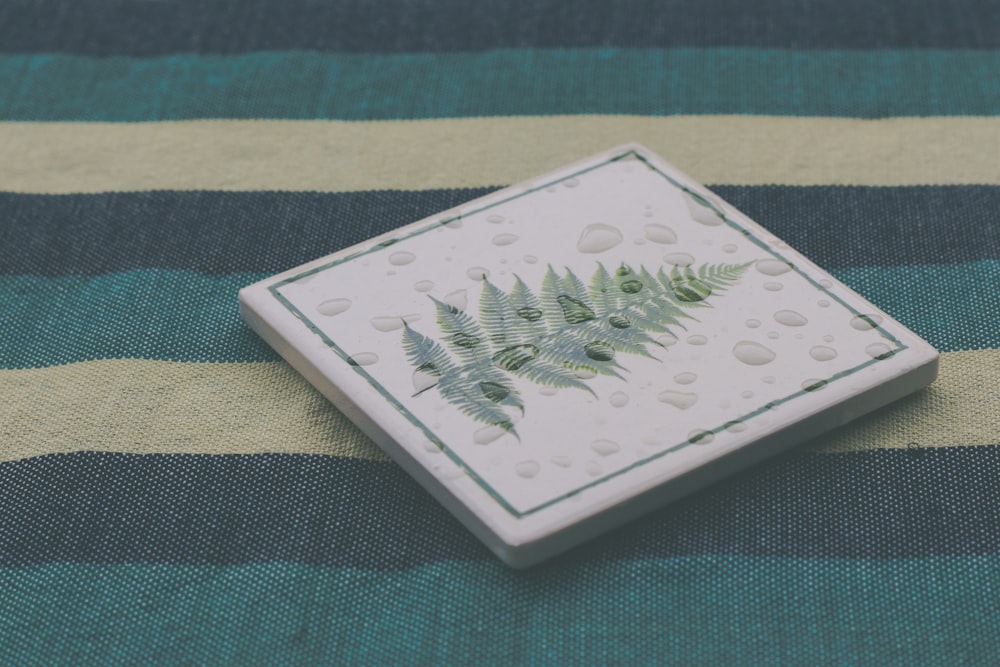 a green and white tile with a fern on it