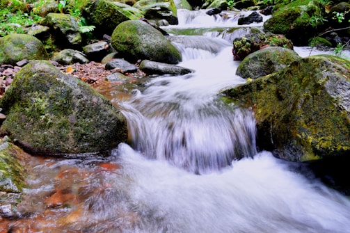 Crystal-clear mountain spring water flowing over smooth stones, the natural source of maqwave’s purity.